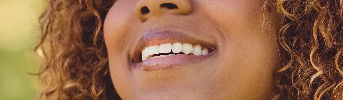 Dentist Canoga Park CA About Us A photo of a woman with warm-toned skin and curly brown hair with a radiant smile, highlighting her healthy, white teeth.