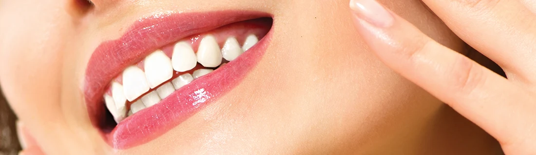 Dentist Canoga Park CA Biomimetric Dentistry A close-up shows a smile with glossy pink lips and bright white teeth while a manicured hand is near their cheek.