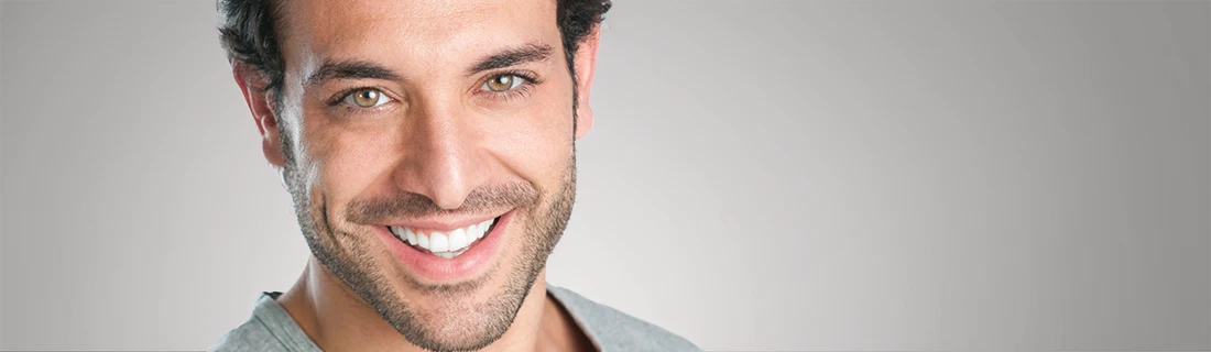 Dentist Canoga Park CA Dental Bonding A smiling man with dark, curly hair, light brown eyes, and a neatly trimmed beard is posed against a muted background.