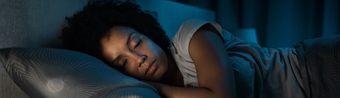 Dentist Canoga Park CA Night Guard A person with dark, curly hair sleeps peacefully with their eyes closed on a patterned pillow in a dimly lit bedroom.