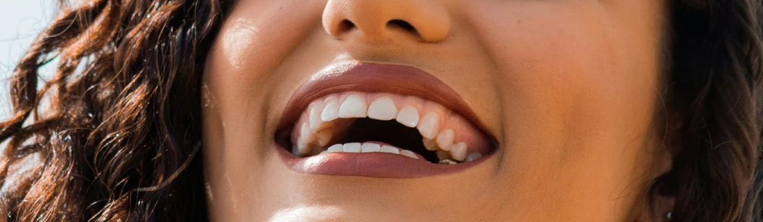 A close-up of a smiling mouth with white teeth and dark curly hair.