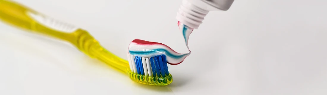 Dentist Canoga Park CA Toothpaste Fluoride Treatment Close-up of a yellow toothbrush with red, white, and blue striped toothpaste being applied from a tube